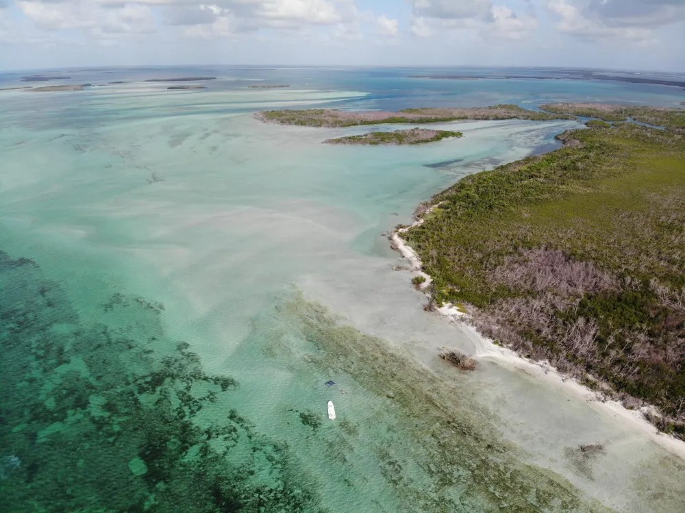 Aerial view of turquoise sea with a boat near a green and brown coastline under cloudy skies.