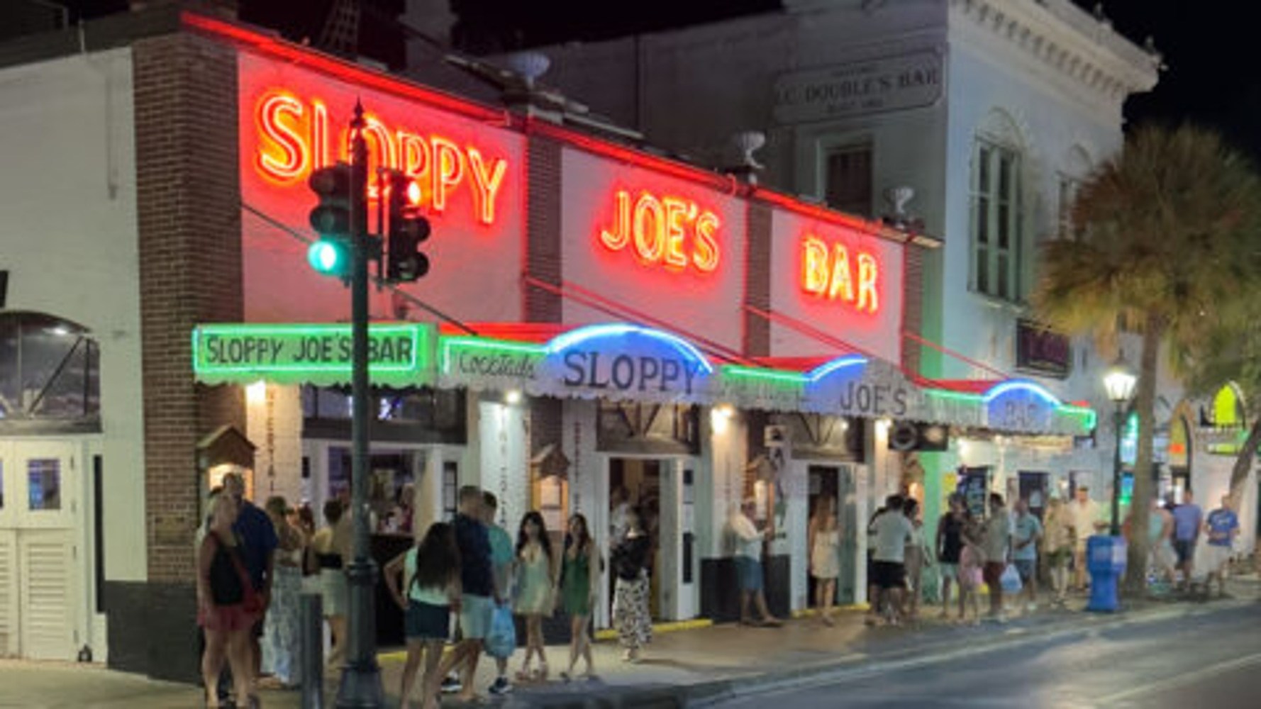 People outside Sloppy Joe's Bar with neon signs at night.