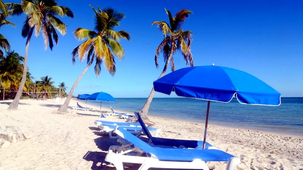 Beach chairs and blue umbrellas at Smathers Beach in Key West with palm trees and calm ocean water sunset watersports